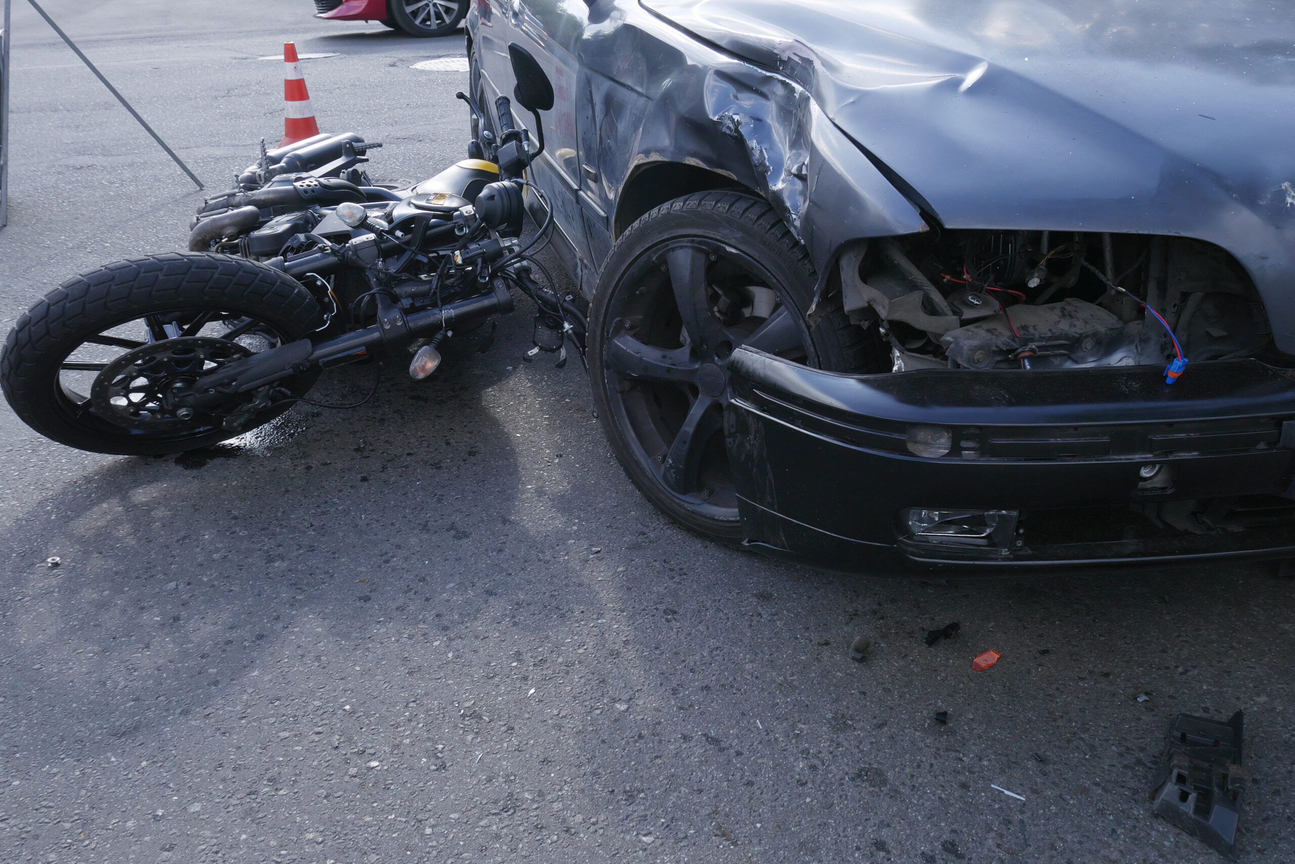 A road accident,a motorcycle lying next to a damaged car with a broken headlight,a warning sign.