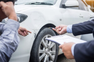 Insurance agent writing on clipboard while examining car after accident claim being assessed and processed