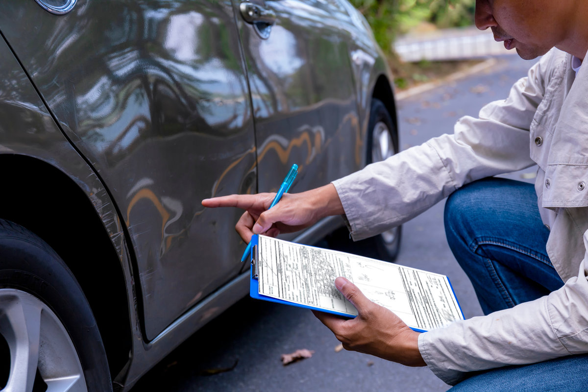 Insurance agent writing on clipboard while examining car after accident claim being assessed and processed. Insurance man check for damage on side door car after accident. Transportation concept