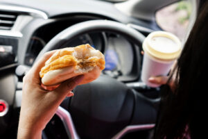 forbidden and perilous with close-up of woman's hand, holding burger and coffee, engaged in reckless eating and drinking While driving car