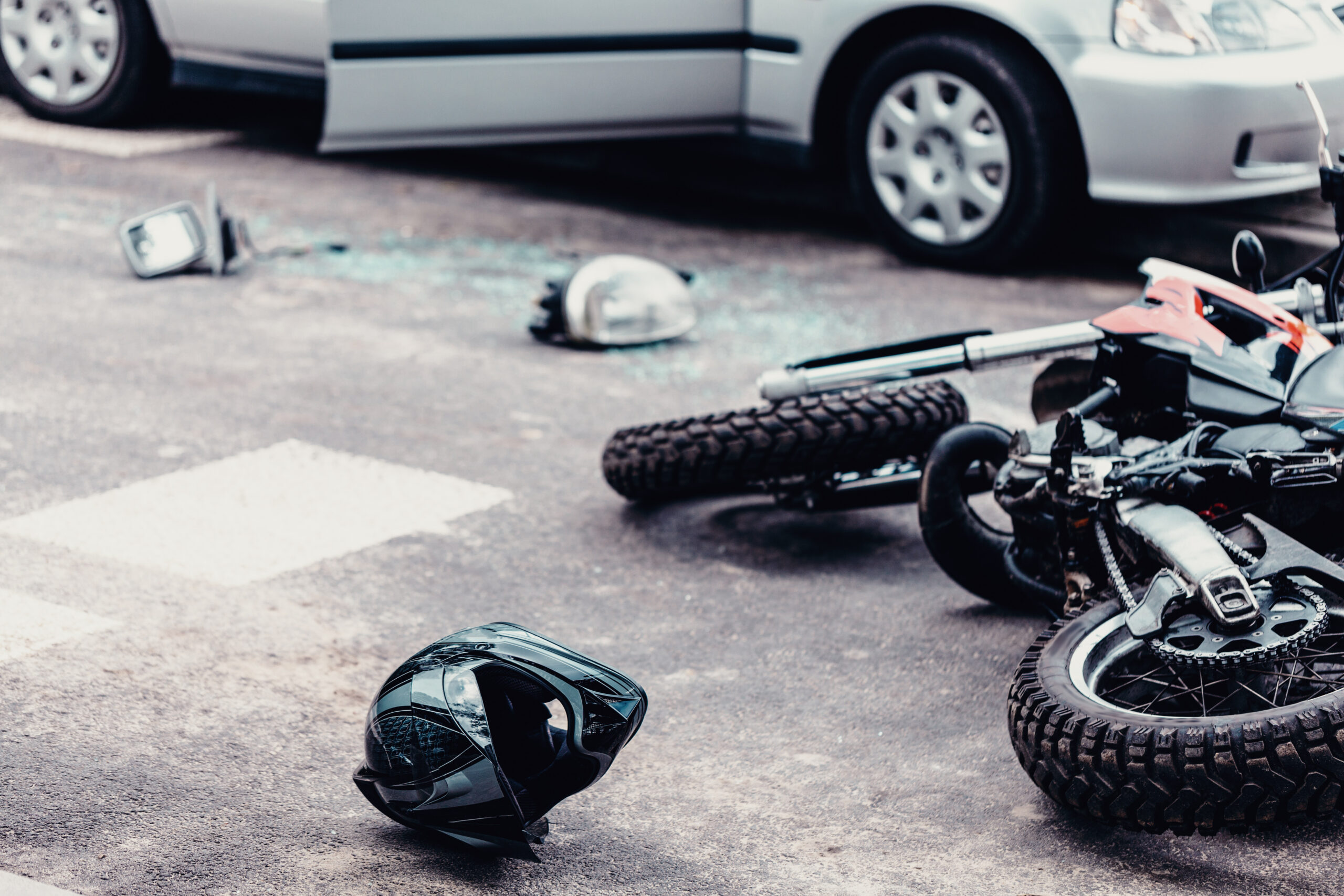 Helmet and motorcycle next to broken peaces of a car on the street after car crash