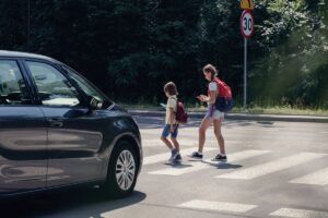 Car in front of children on pedestrian crossing walking from the school and looking at their smartphones